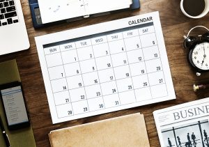 desktop with calendar, newspaper, computer, diary, cell phone, alarm clock